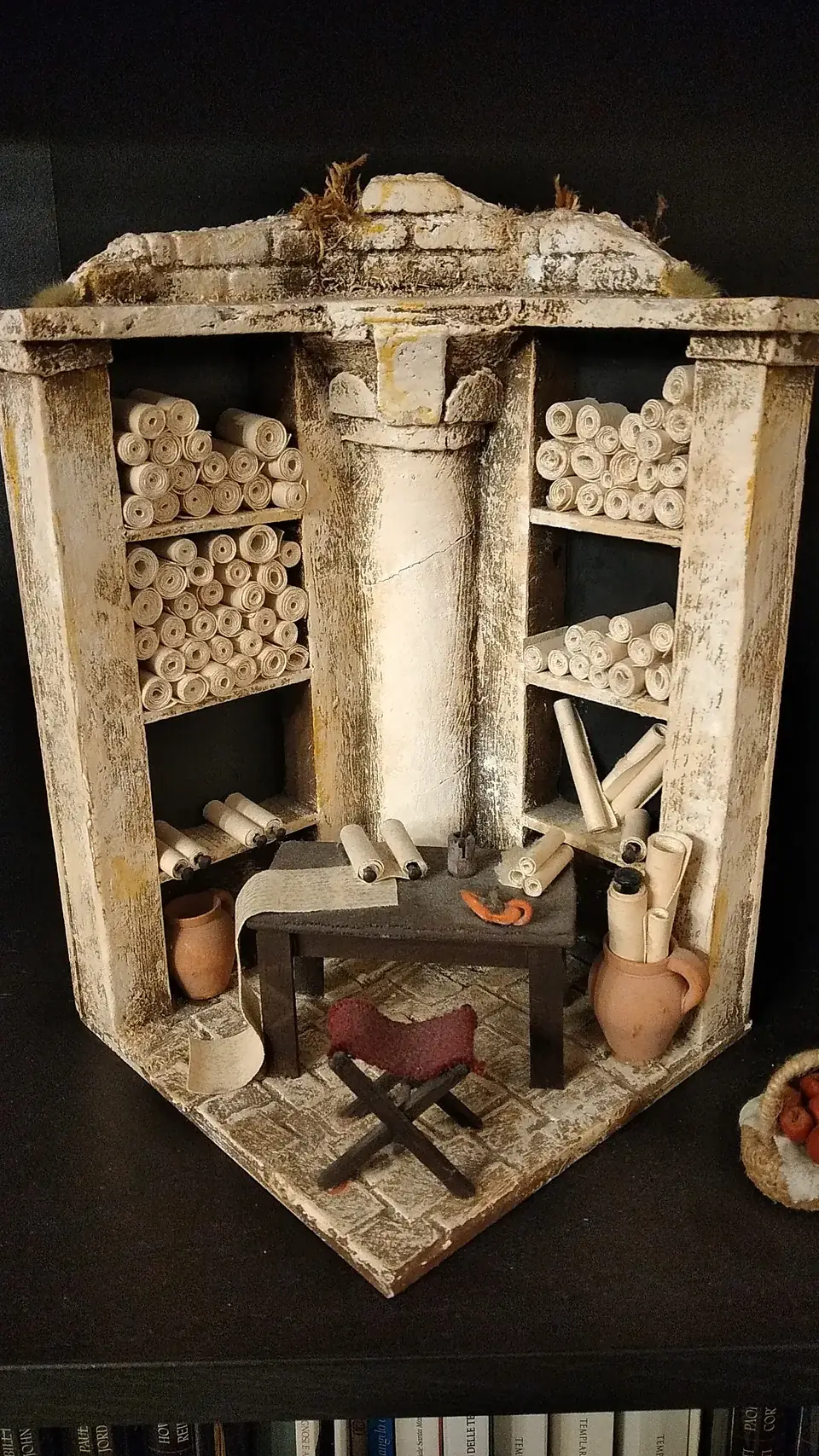 Diorama in miniatura di una biblioteca antica con colonne, scaffali di rotoli e arredi in scala